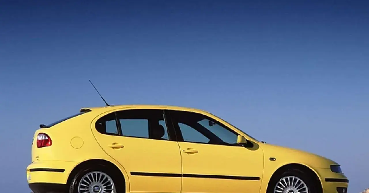 Żółty Seat Leon 2000, sportowy hatchback, zaparkowany na tle błękitnego nieba.