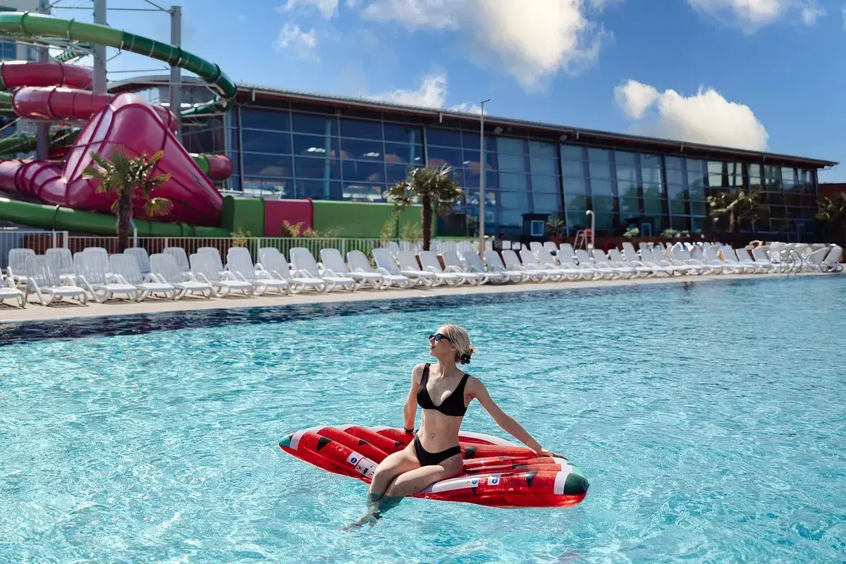 Frau entspannt auf aufblasbarem Kissen im Pool des Aquaparks Breslau, im Hintergrund Wasserrutschen und Liegestühle.