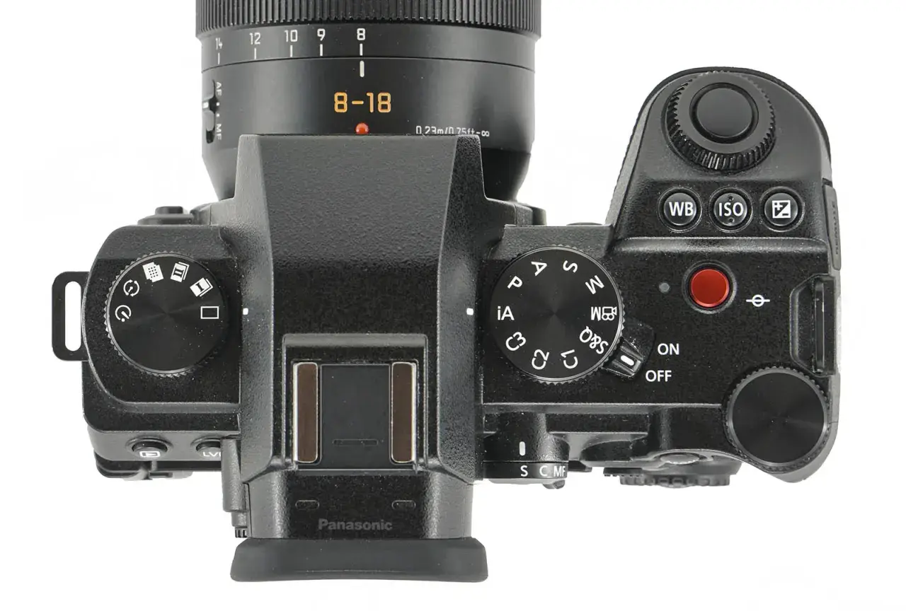Górna część aparatu Panasonic Lumix G9 II z obiektywem 8-18 mm. Widoczne pokrętła trybów, przyciski i ekran.