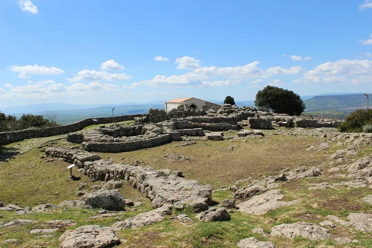 Rovine del santuario nuragico di Santa Vittoria sotto un cielo azzurro con nuvole bianche.