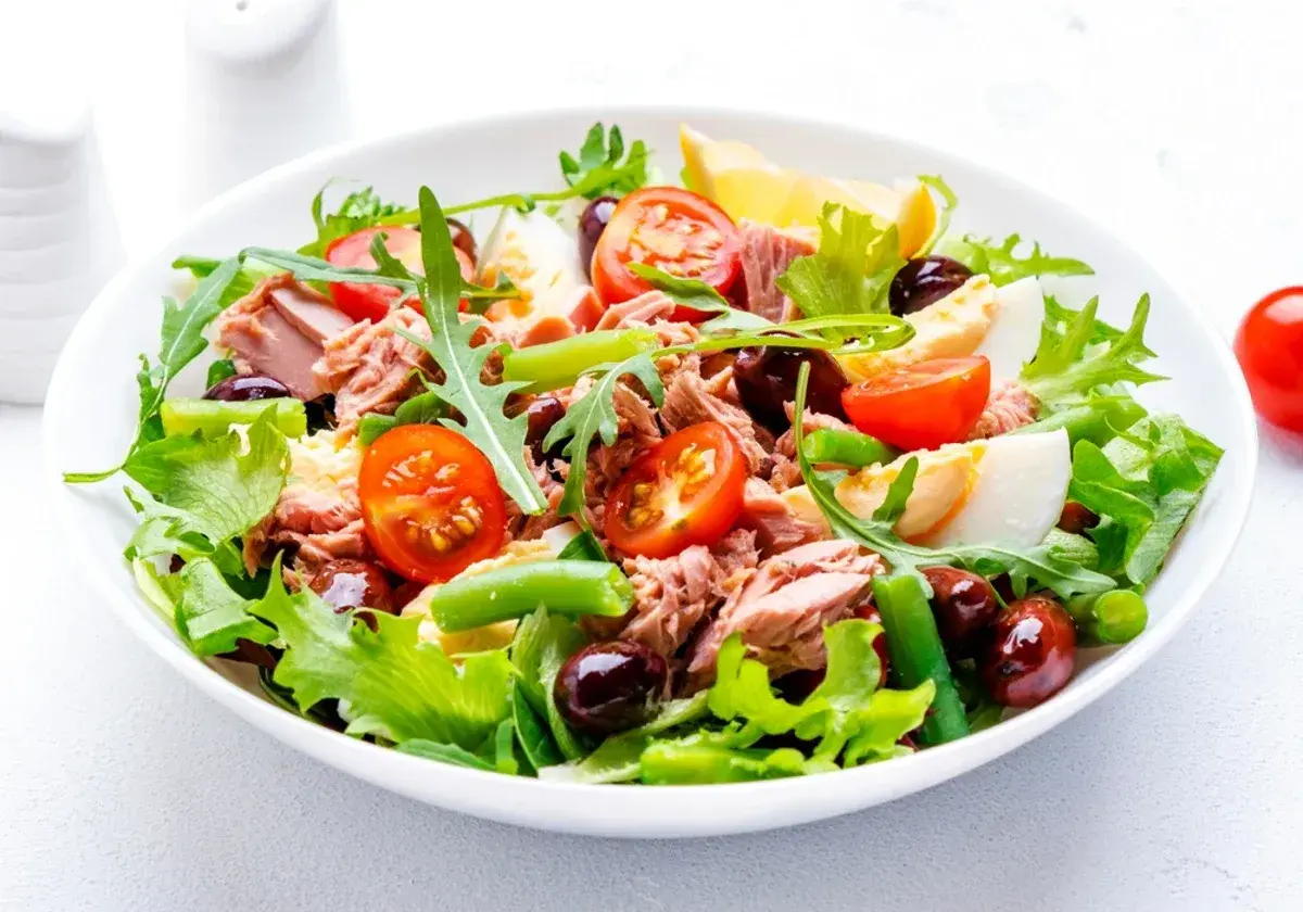 En fräsch sallad nicoise med tonfisk, ägg, tomater, oliver och gröna bönor på en bädd av sallad.