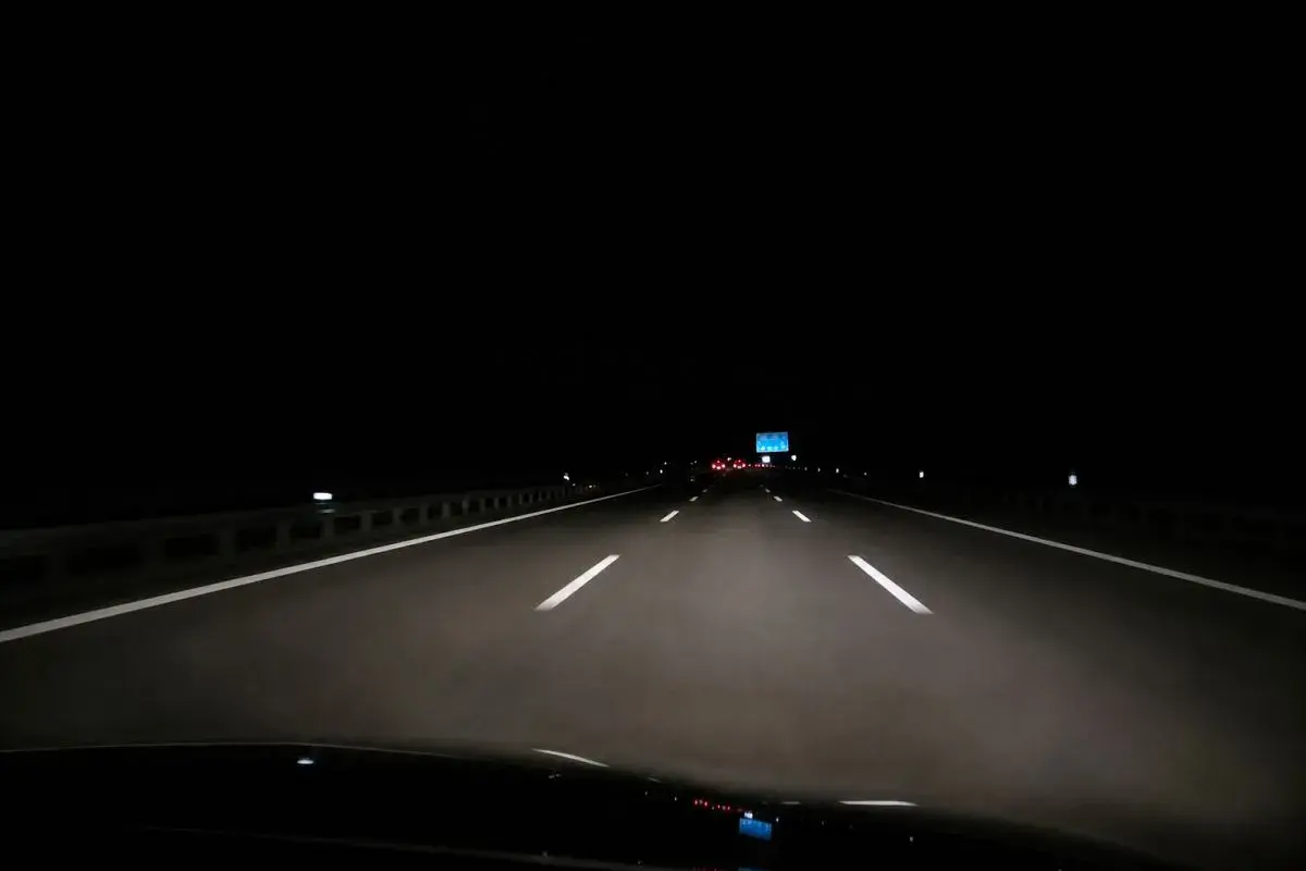 Fahrt über die Autobahn nachts. Scheinwerfer beleuchten die Fahrbahn, weiße Linien weisen den Weg in die Dunkelheit.