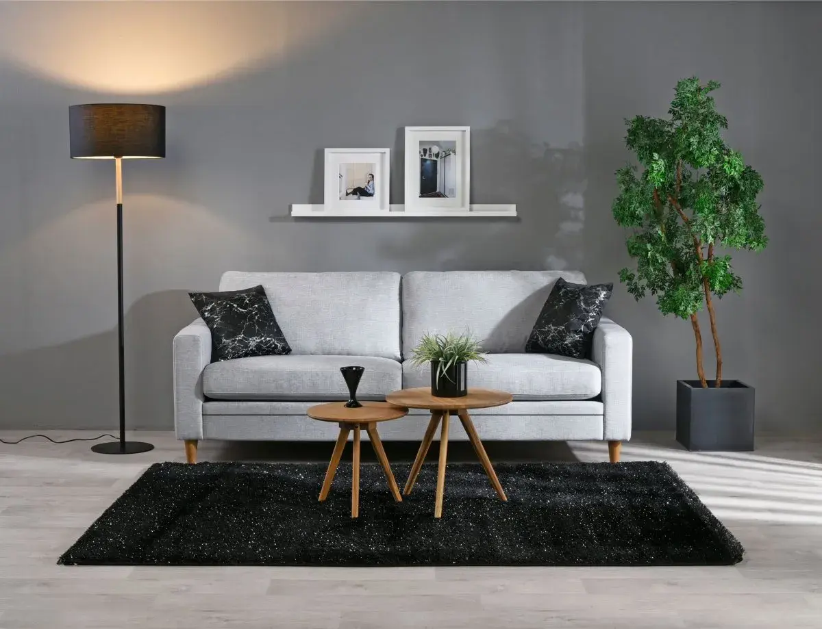 Grå soffa med svarta marmorkuddar, två runda träbord, svart matta och golvlampa i modern stil.