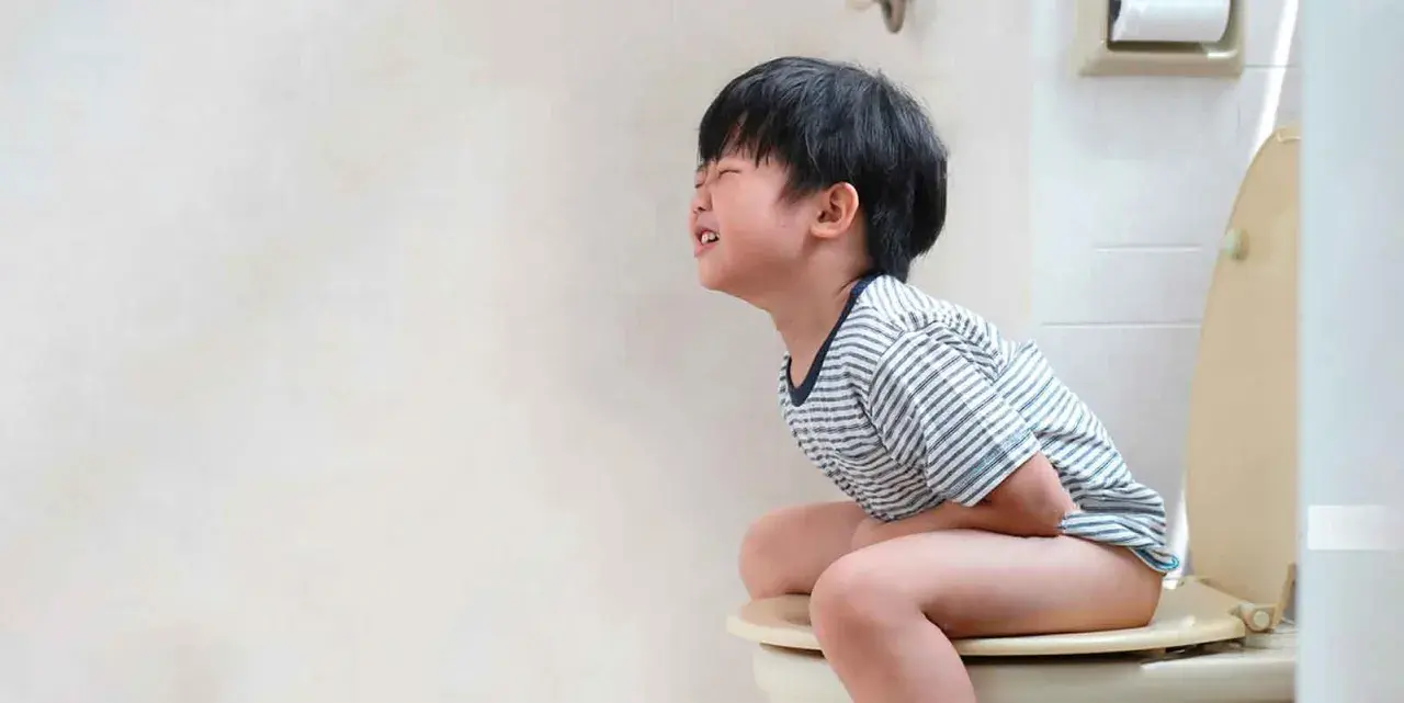 Niño de 5 a 10 años con estreñimiento, sentado en el inodoro con dolor y esfuerzo.