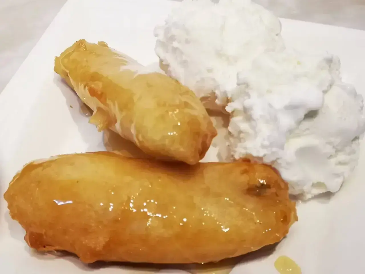 Två gyllene friterade bananer med honung serveras med en generös klick vaniljglass. En ljuvlig dessert!