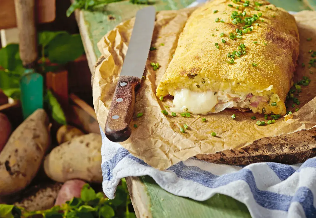 Herzhaft gefüllte polpette di patate, goldbraun paniert, mit geschmolzenem Käse im Inneren. Frische Kartoffeln liegen daneben.