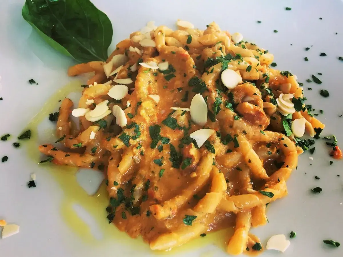 Busiate alla trapanese, un piatto di pasta siciliana con un sugo ricco, guarnito con mandorle a lamelle e prezzemolo fresco.