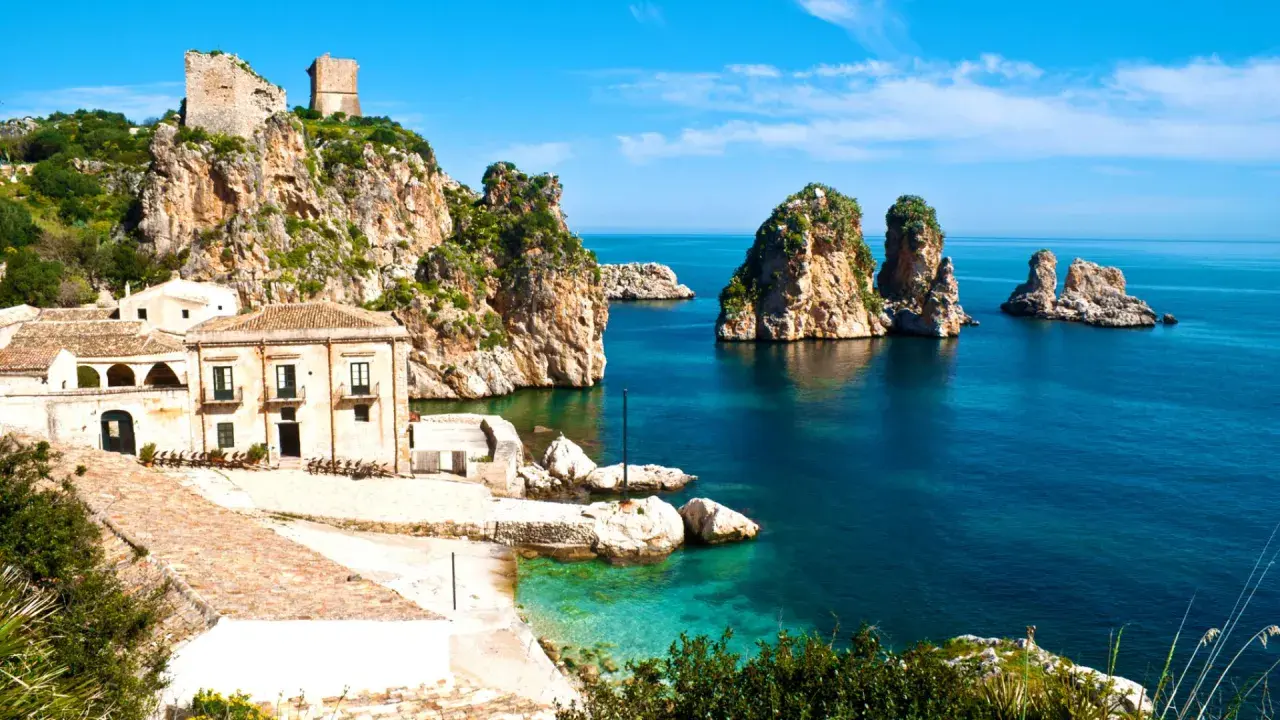 Torri e case antiche su scogliere rocciose, con faraglioni nel mare blu. Un paesaggio che evoca la storia dei bizantini in Sicilia.