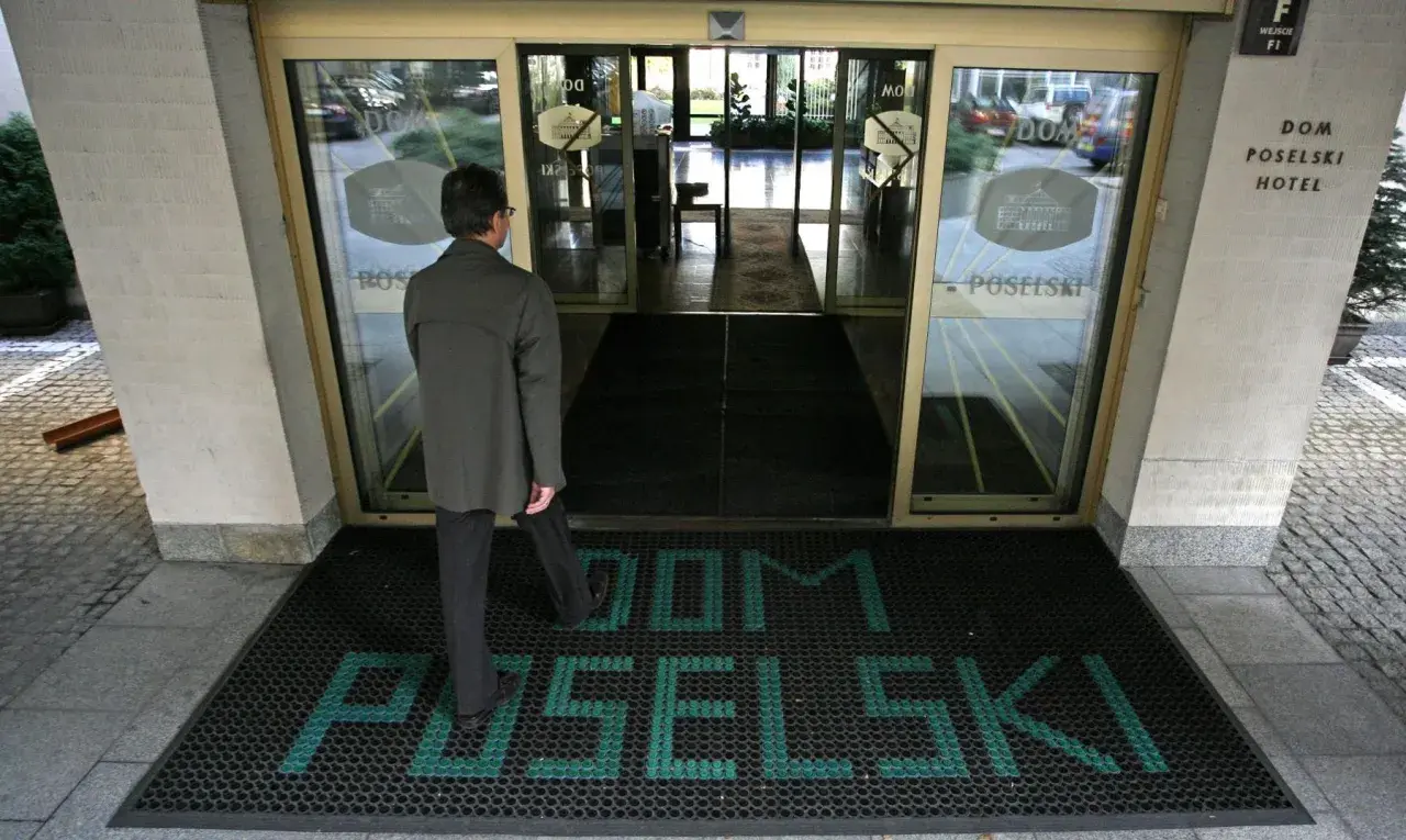 Mężczyzna wchodzi do hotelu poselskiego. Na wycieraczce przed wejściem widnieje napis "DOM POSELŚKI".
