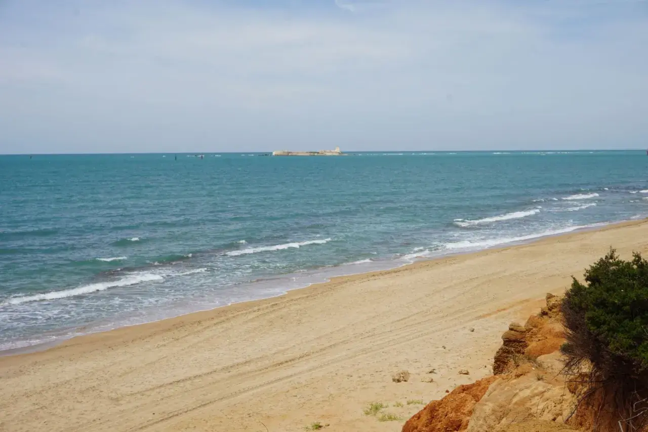 Playa de arena dorada con mar turquesa y una estructura en el horizonte. Un rincón idílico de las calas Chiclana.