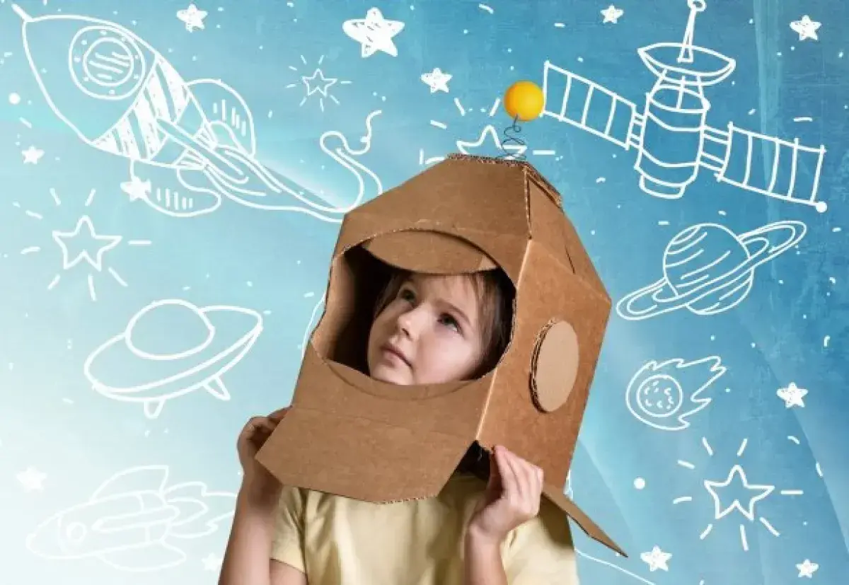 Dziecko w kartonowym hełmie astronauty patrzy w górę, otoczone rysunkami rakiet i planet. To właśnie takie marzenia o kosmosie napędzają nas do odkrywania.