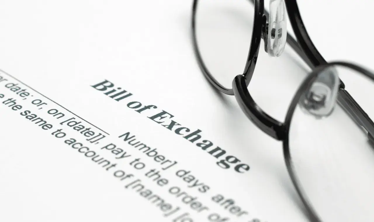 Okulary leżą na dokumencie "Bill of Exchange". To jest weksel, czyli papier wartościowy, który zobowiązuje do zapłaty określonej sumy pieniędzy.