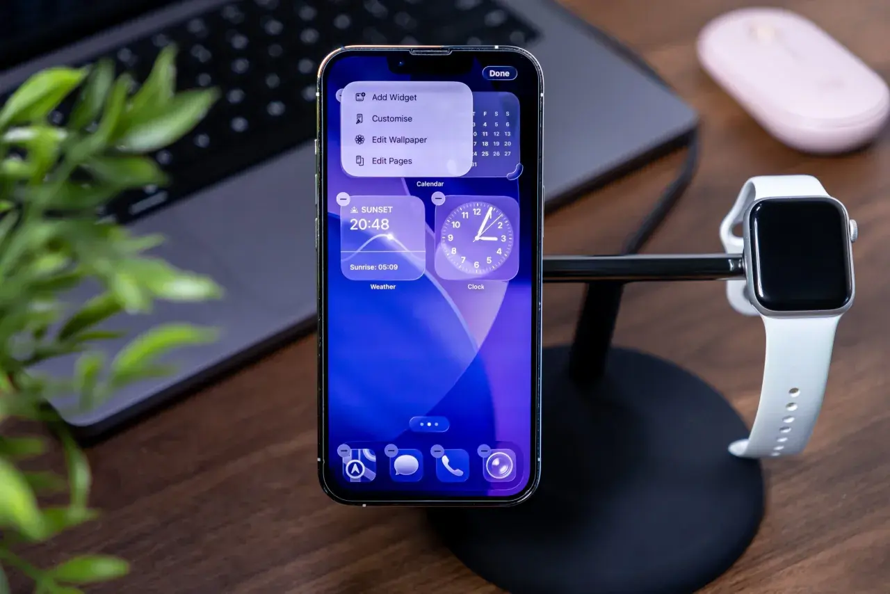 Nowy iPhone z najnowszym iOS, pokazujący widżety pogody i zegara. Obok stoi Apple Watch.