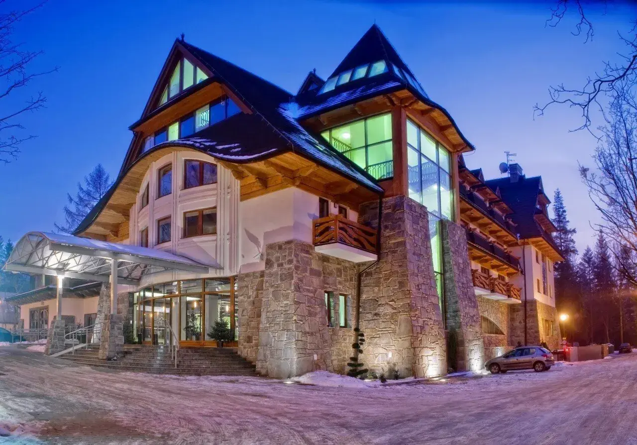Elegancki hotel Crocus w zimowej scenerii, z kamienną fasadą i drewnianymi elementami, oświetlony nocą.