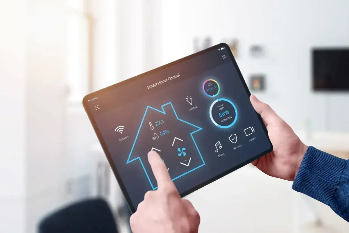 Une main utilise une tablette pour contrôler une application domotique gratuite. L'interface affiche la température, la lumière et d'autres fonctions de la maison.