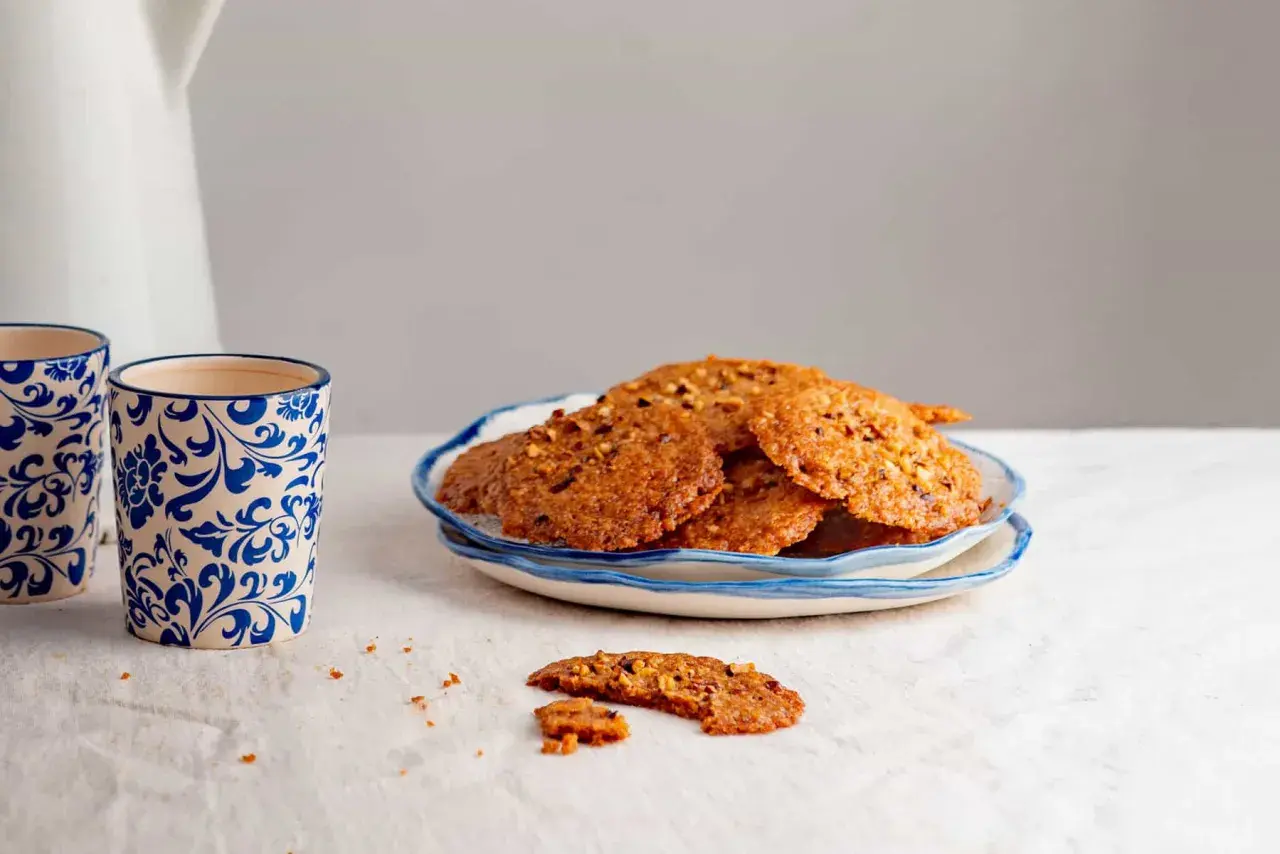 Deliciosas galletas de jengibre crujientes con trozos de nueces, servidas en un plato azul y blanco.
