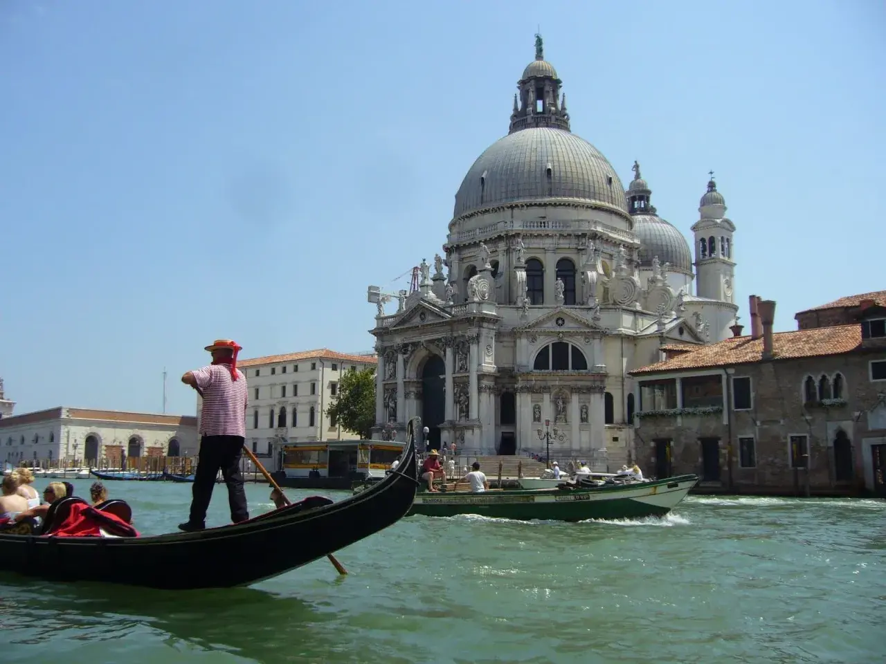 Gondolier wita turystów w Wenecji. W tle Bazylika Santa Maria della Salute i kanał.