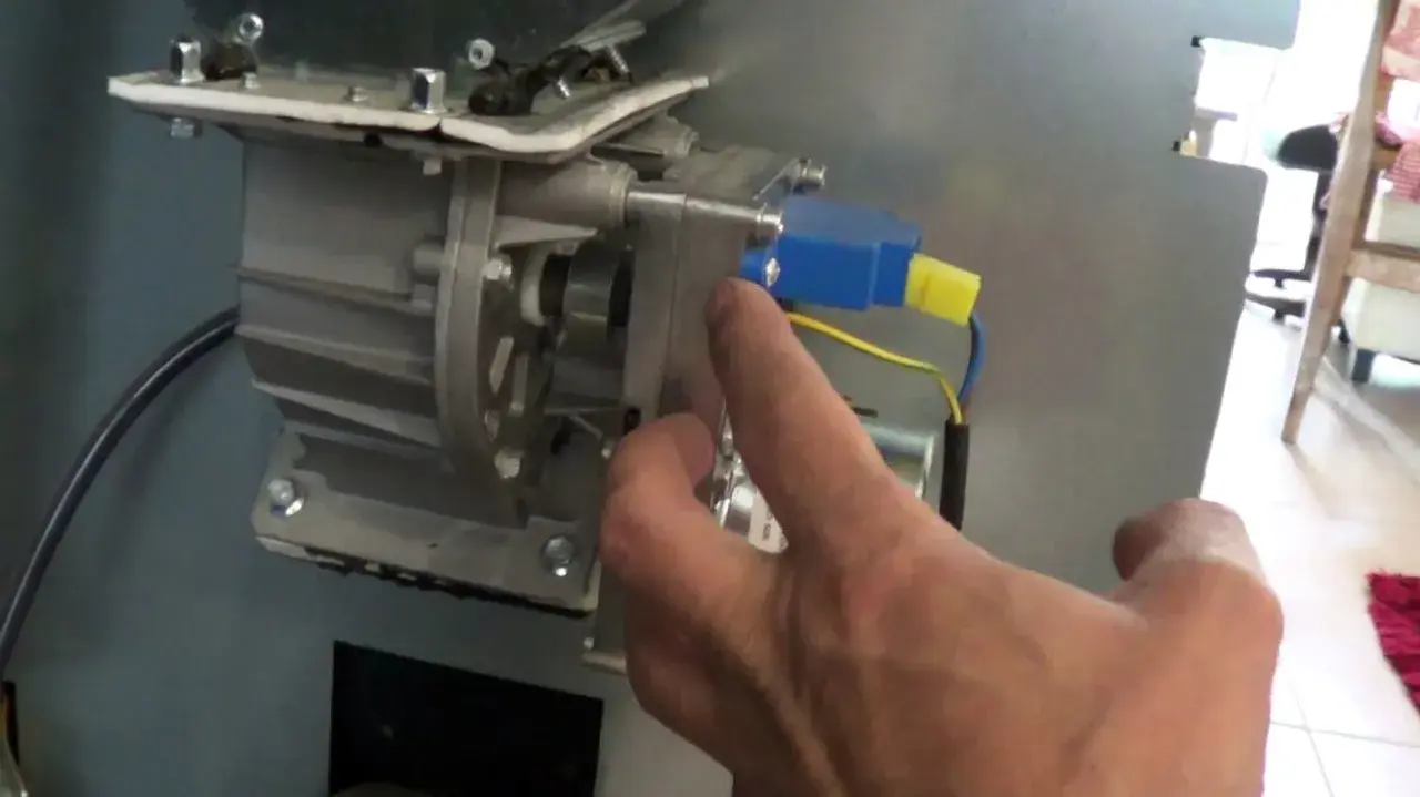 Main d'un homme manipulant le mécanisme d'un poêle à granulés, pour nettoyer le pressostat.