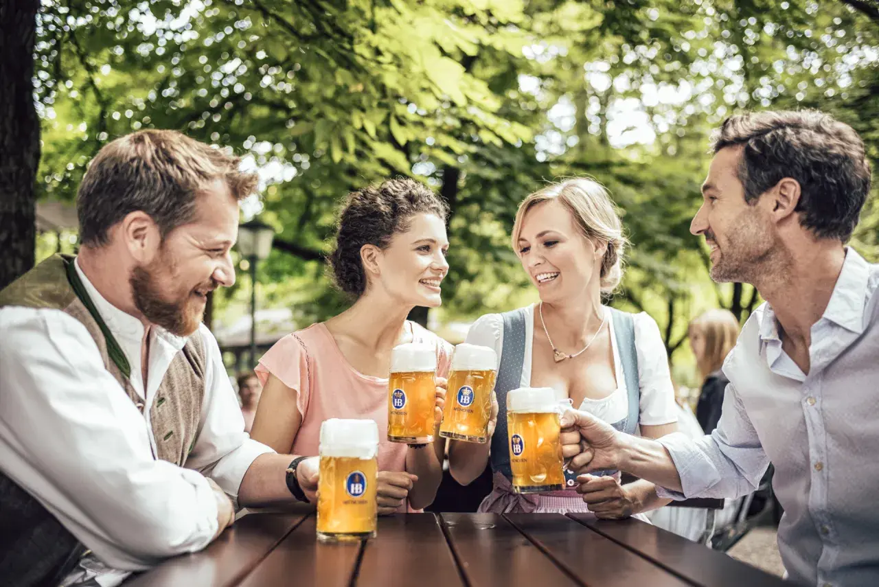 Coppie brindano con boccali di zwickl birra sotto alberi verdi.