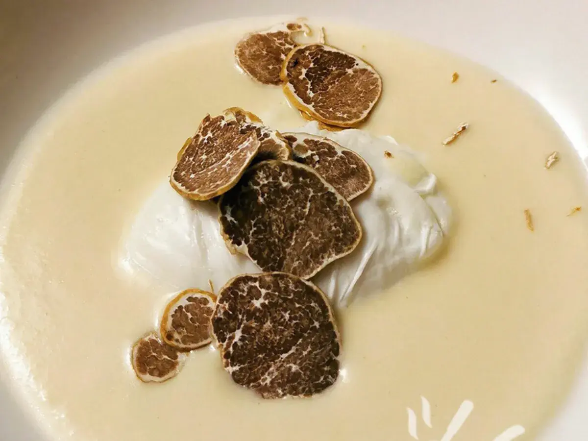 Uovo pochè su una cremosa fonduta, guarnito con scaglie di tartufo nero. Un piatto raffinato e profumato.
