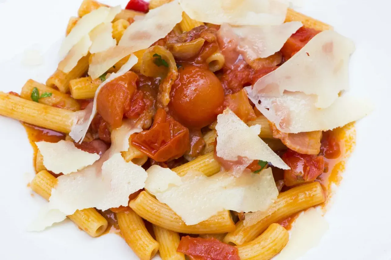 Piatto di rigatoni conditi con un ricco sugo amatriciana, pomodorini, guanciale e scaglie di pecorino.