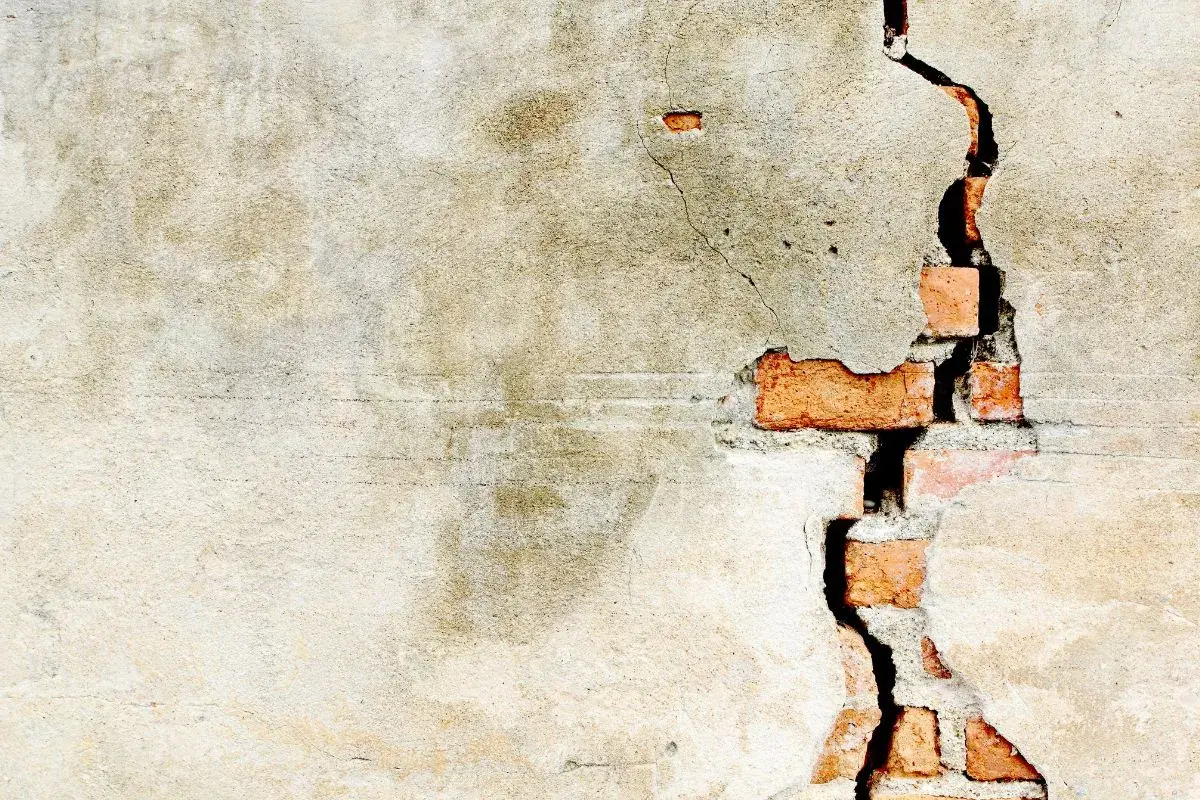 Crepe intonaco interno rivela mattoni rossi. La parete mostra segni del tempo e usura.