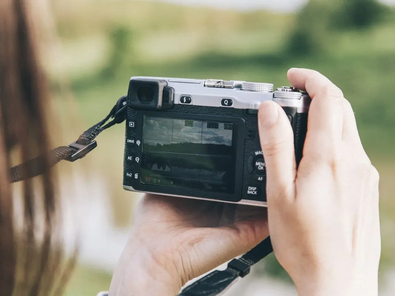 Dłonie trzymają aparat, który może być dobrym aparatem fotograficznym do 500 zł. Na ekranie widać krajobraz.