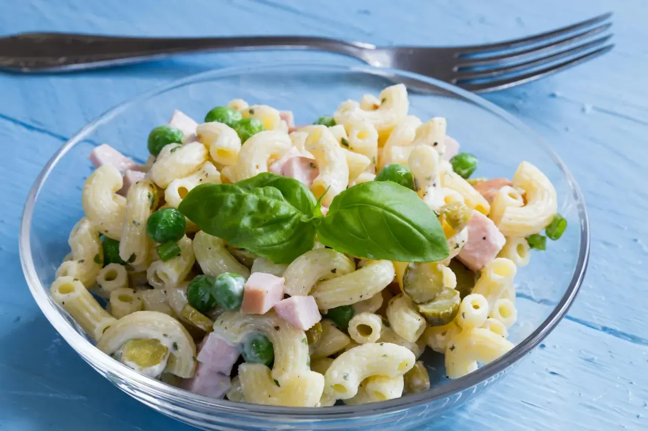 Ein cremiger Nudelsalat mit Erbsen, Schinken und Gurken, garniert mit Basilikum. Perfekt als schnelles rezept nudelsalat.