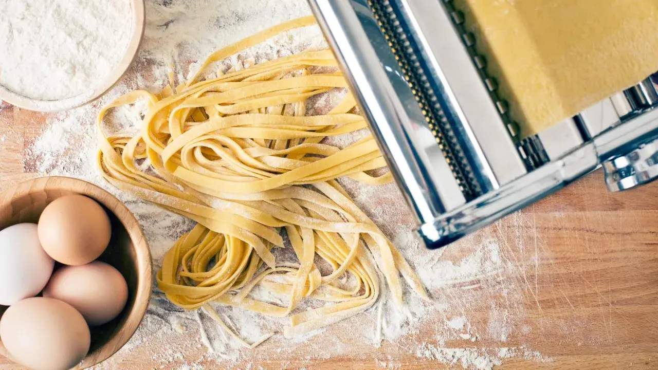 Frischer Tagliatelle-Nudelteig mit Eiern, Mehl und Nudelmaschine auf Holzbrett.