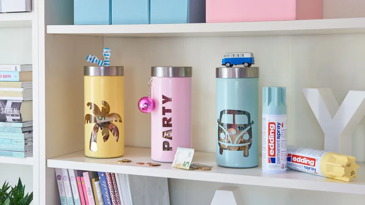 Kolorowe skarbonki DIY z motywami palmy i busa. Na półce obok stoją puszki z farbą w sprayu.