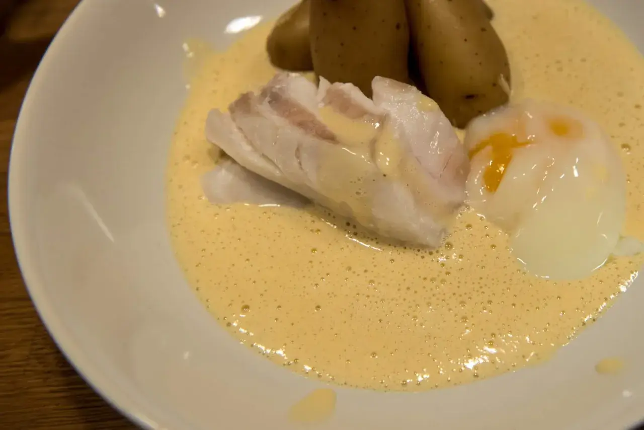 En portion torskrygg med pocherat ägg och potatis i en krämig sås. Perfekt för en middag med vin till torskrygg.