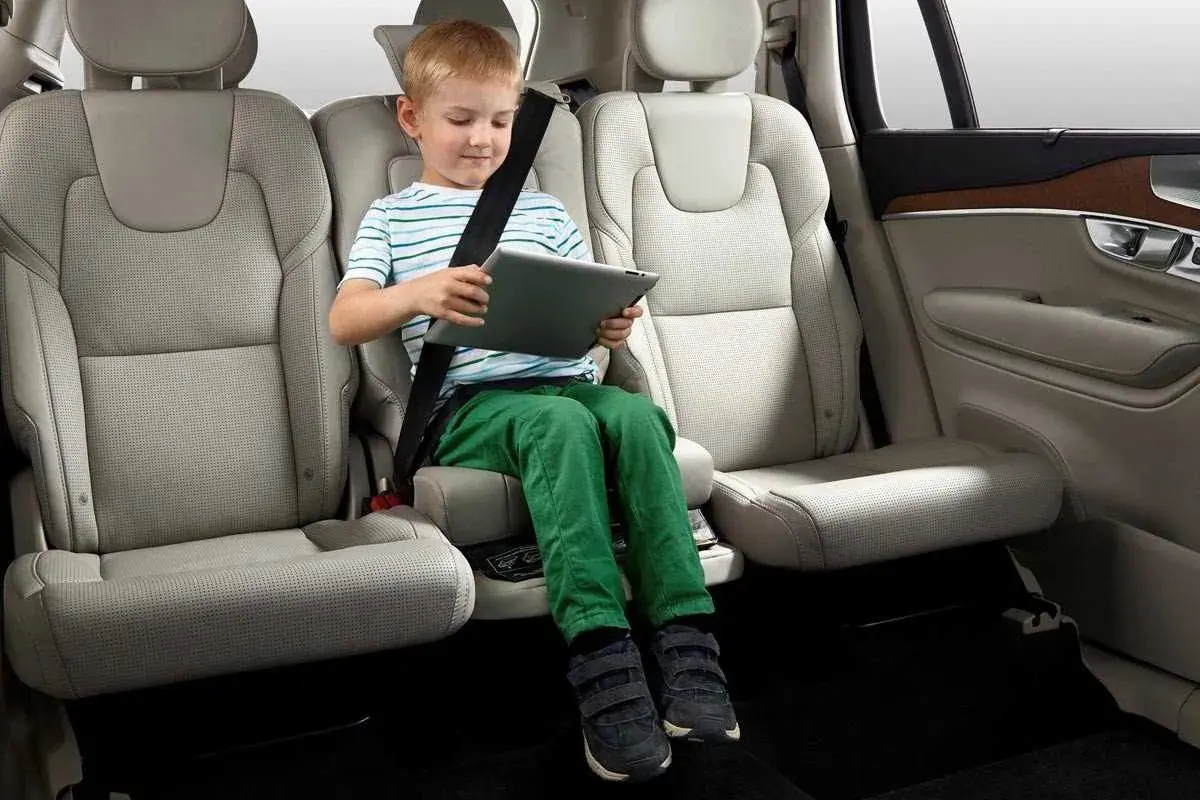 Niño en alzador coche, cumpliendo la normativa de seguridad vial. Viaja entretenido con su tablet.