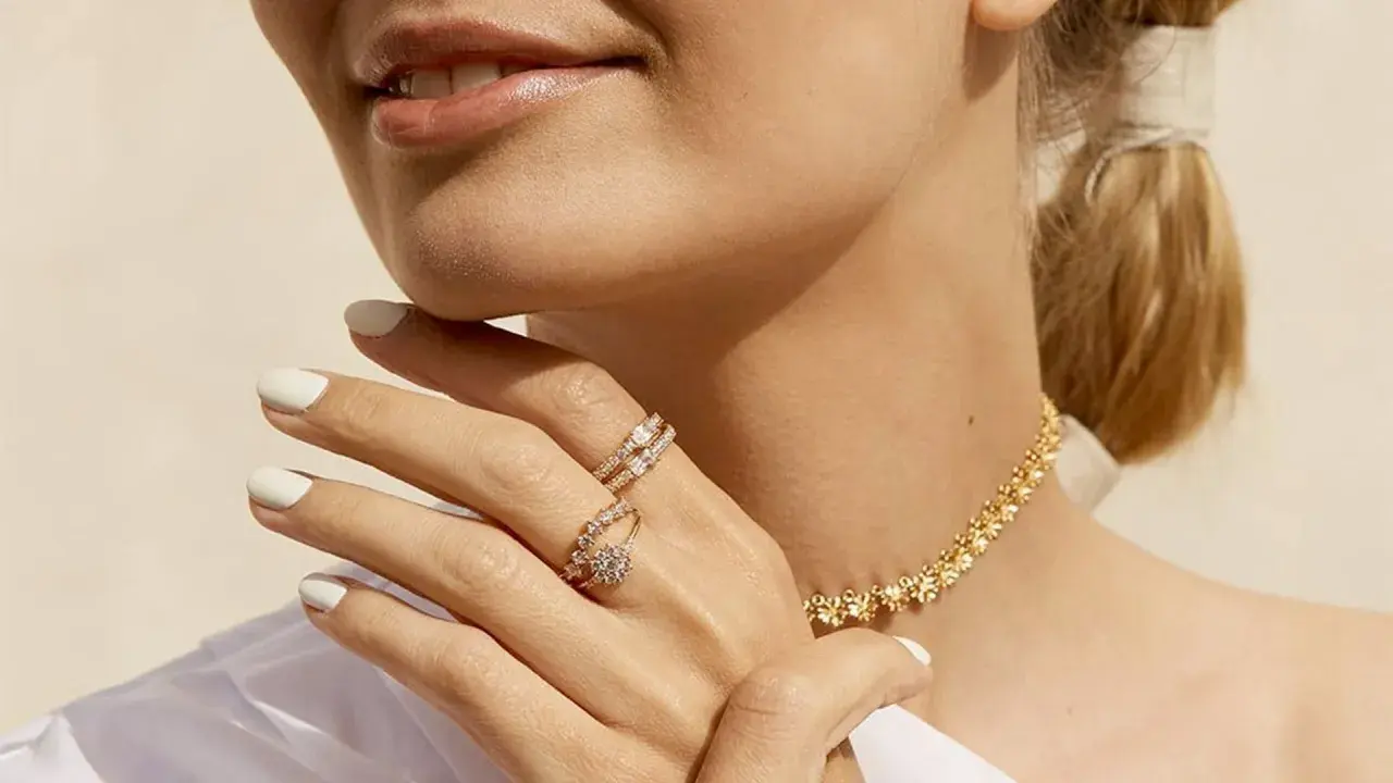 Manos con manicura blanca luciendo dos anillos de **joyería Suárez anillos** y un collar dorado.