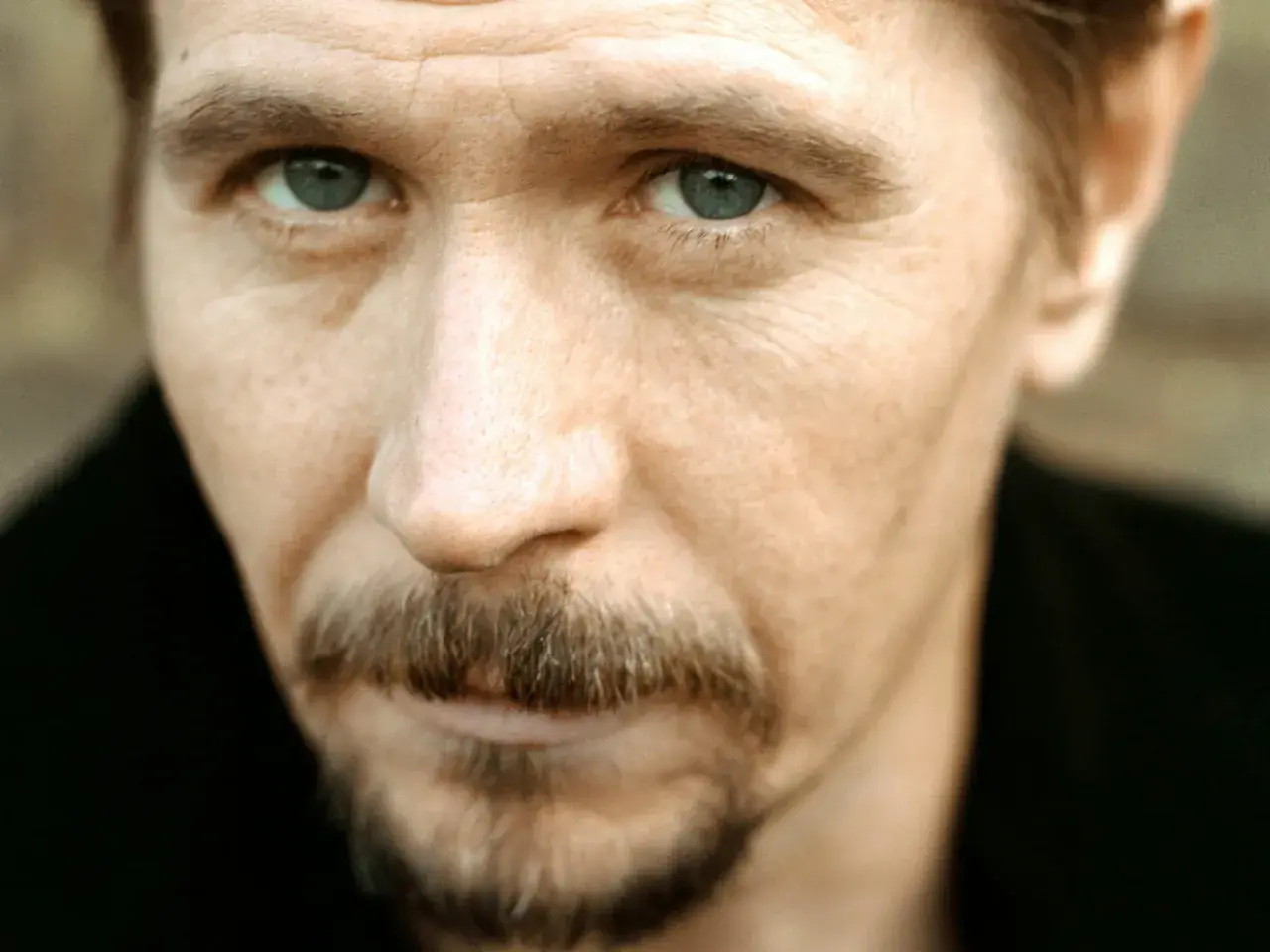 Młody Gary Oldman z przenikliwym spojrzeniem i charakterystycznym wąsikiem.