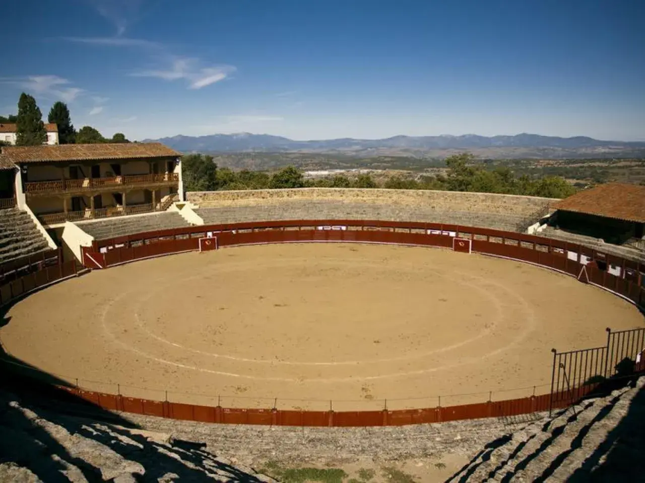 La plaza de toros El Castañar, con su arena de arena y gradas de piedra, se alza majestuosa ante un paisaje montañoso.
