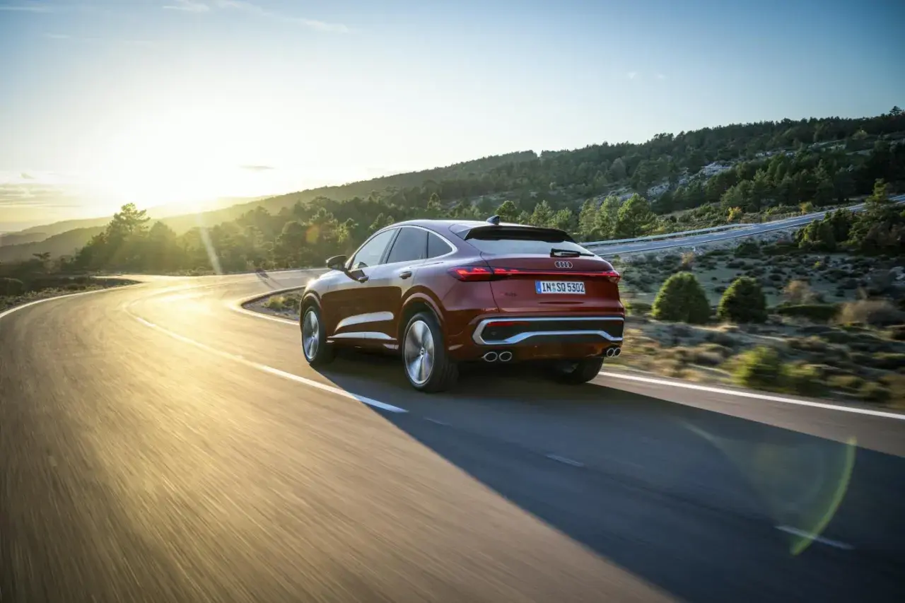 Czerwony samochód Audi coupe na krętej drodze w górach o zachodzie słońca.