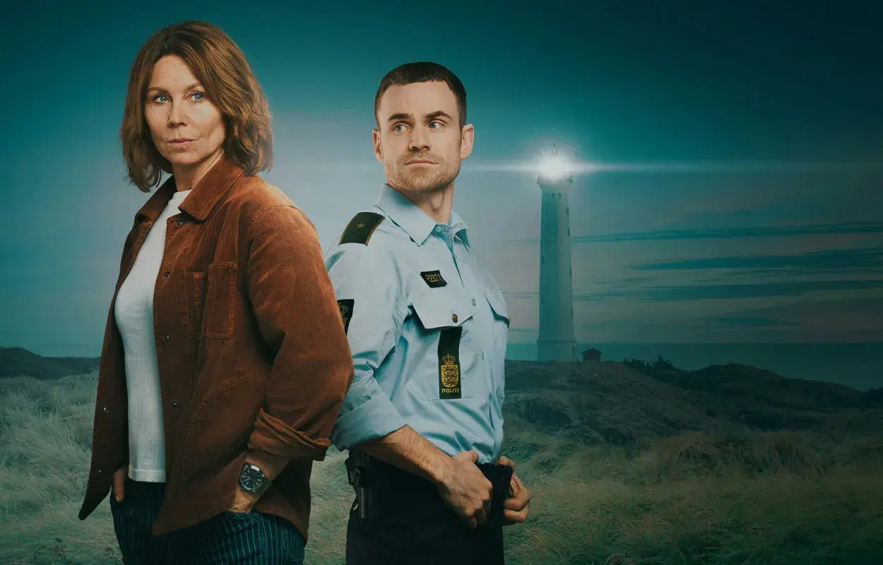 Två poliser står på en kulle med vit sand. I bakgrunden syns ett fyrhus vid havet.