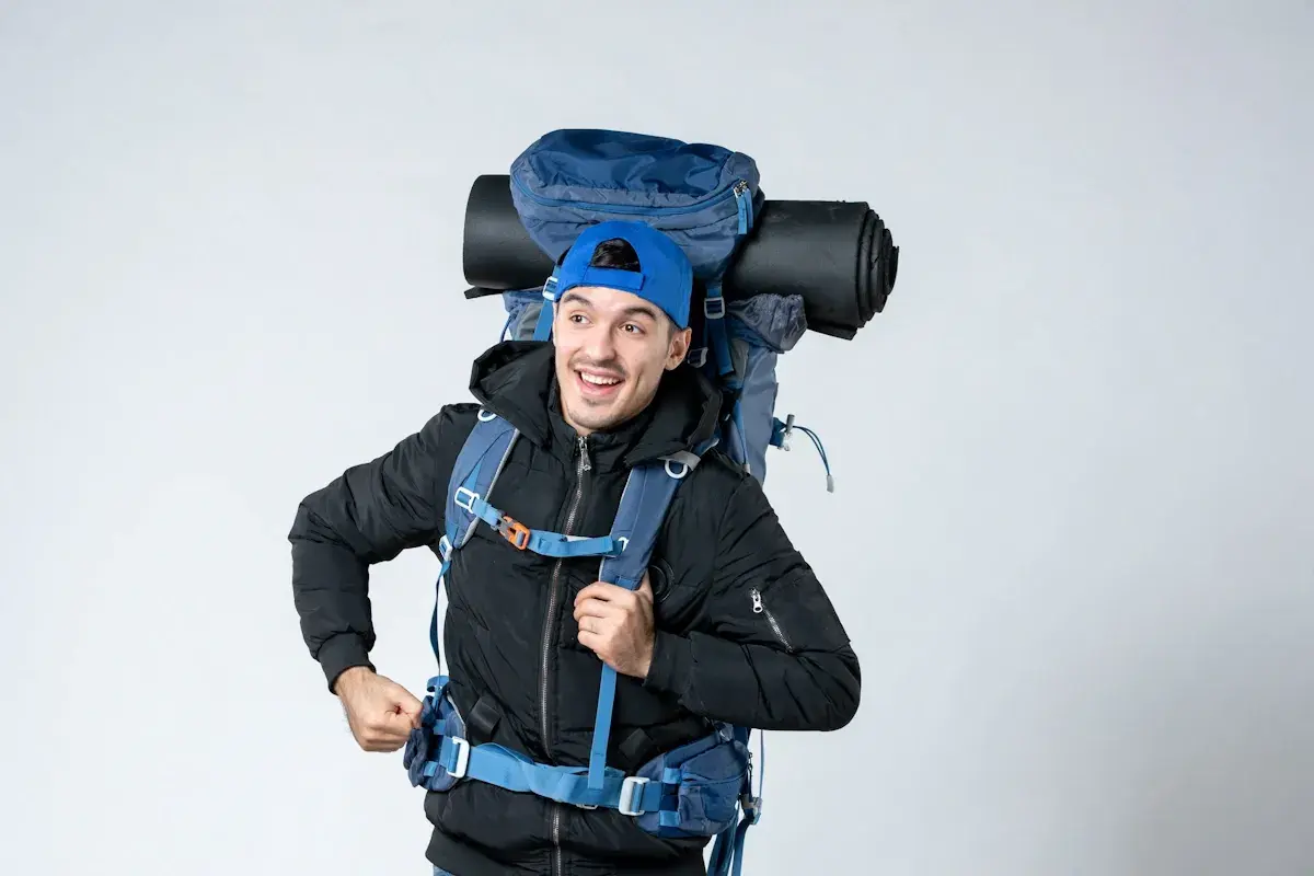 Un jeune homme souriant avec un grand sac à dos bleu, prêt pour l'aventure. On se demande : sac 70 litres combien de kilos ?
