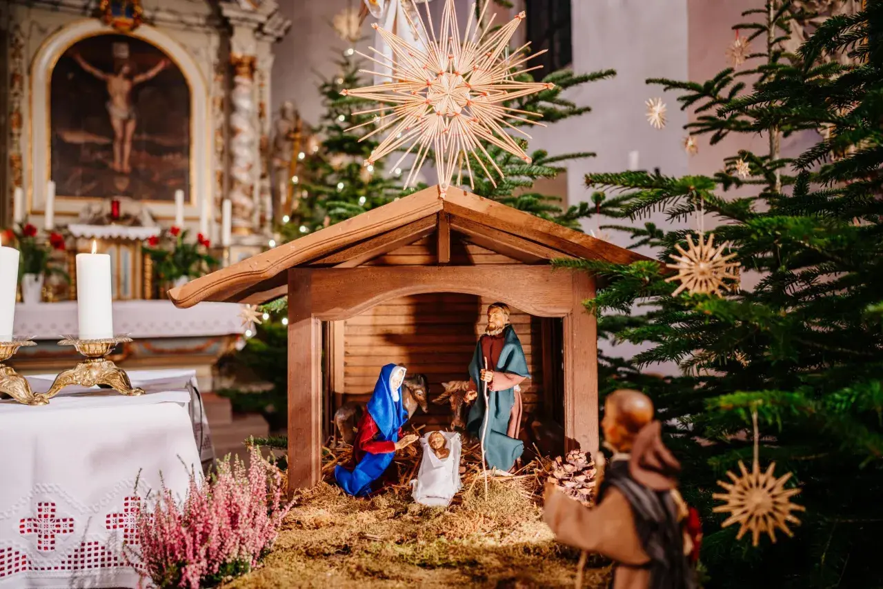 Krippe in einer Kirche, die zeigt, was ist Weihnachten: Maria, Josef und das Jesuskind. Weihnachtsbäume und Kerzen schmücken den Altarraum.