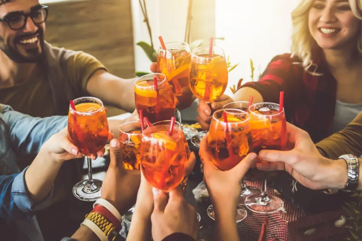 Freunde stoßen mit Aperol Spritz an. Eine bunte longdrinks liste für einen schönen Abend.