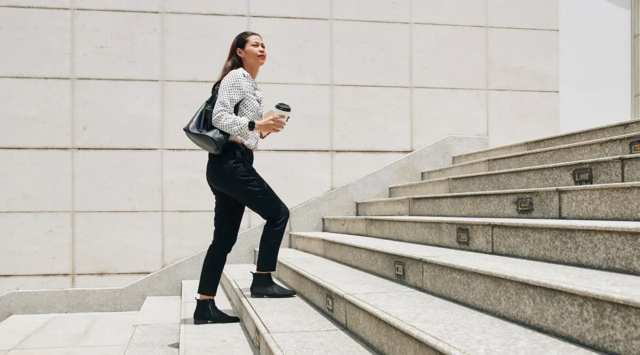 Frau steigt Treppen hoch, Kaffee in der Hand. Ein guter Weg, um abzunehmen durch gehen und fit zu bleiben.