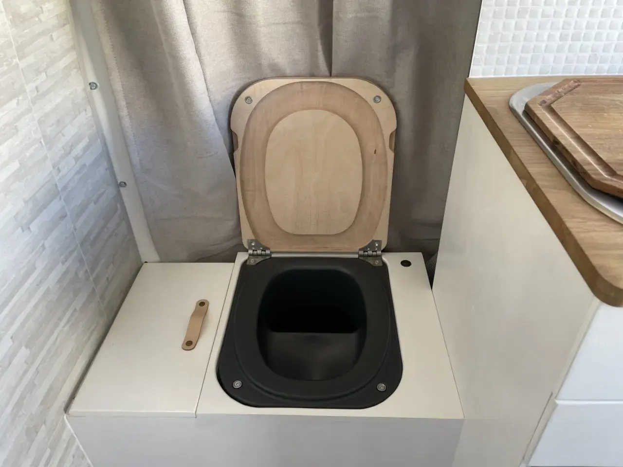 WC de camping aménagé avec abattant en bois et cuvette noire.
