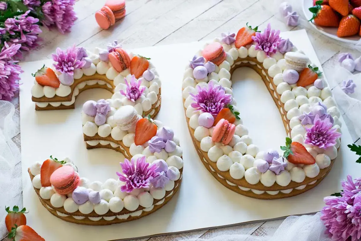 Una torta numero 30 decorata con panna, fragole, macarons e fiori viola.