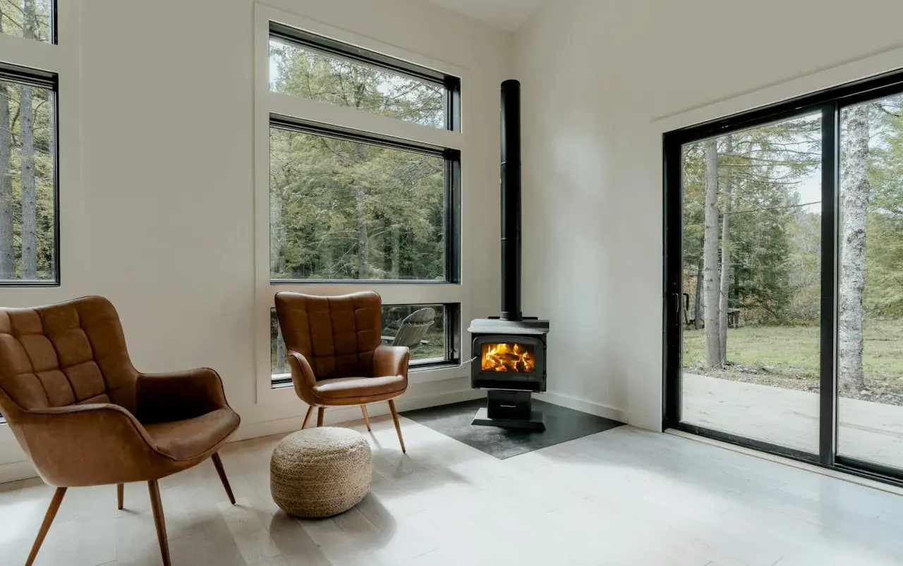 Un poêle à granule appartement, avec deux fauteuils en cuir marron et une vue sur la forêt.