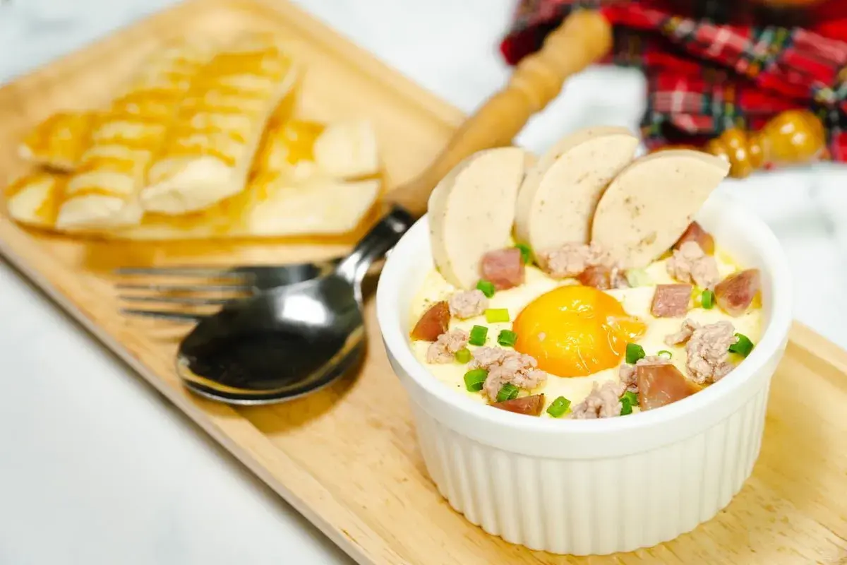 Un œuf cocotte bain-marie, garni de saucisse et de viande hachée, servi avec des bâtonnets de pain grillé.
