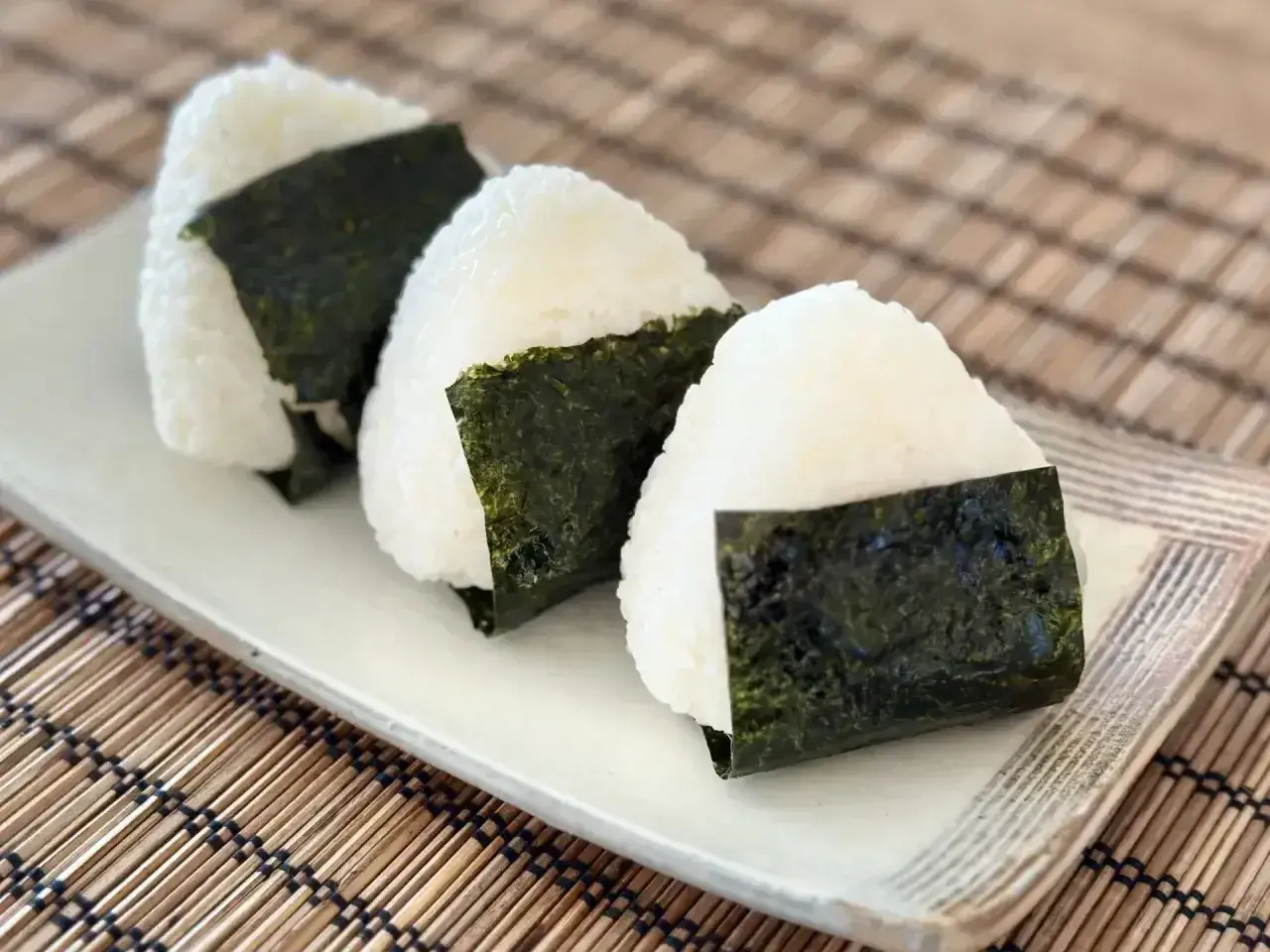 Trzy pyszne onigiri, czyli japońskie kulki ryżowe zawinięte w nori, leżą na talerzu.