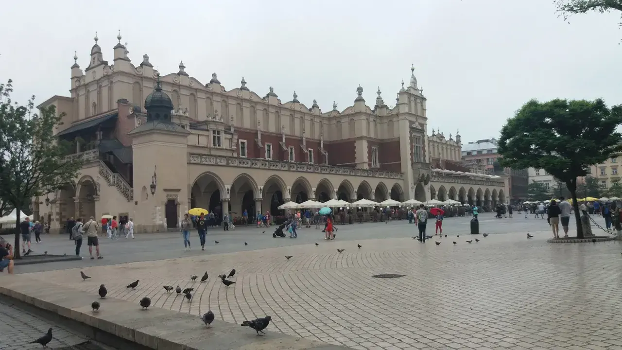 Deszczowy dzień na Rynku Głównym w Krakowie. Ludzie z parasolami spacerują, szukając schronienia w Sukiennicach lub kawiarniach. To świetny pomysł, co robić w Krakowie, gdy pada.