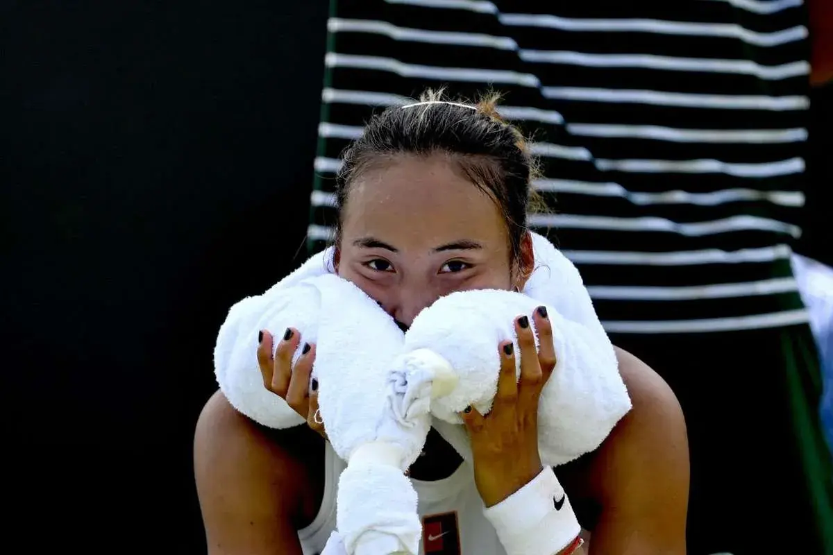 Zmęczona zawodniczka zheng tennis wyciera twarz ręcznikiem.