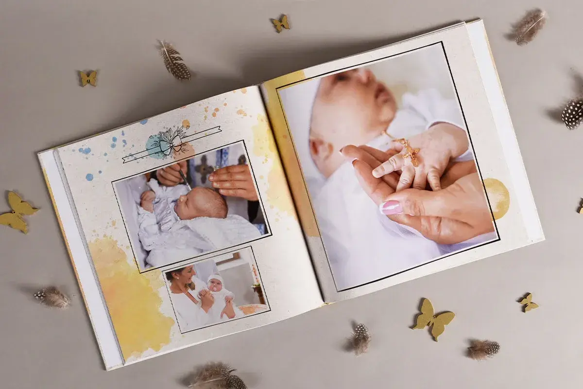 Otwarta księga pamiątkowa z fotografiami niemowlęcia, ozdobiona piórkami i motylkami.