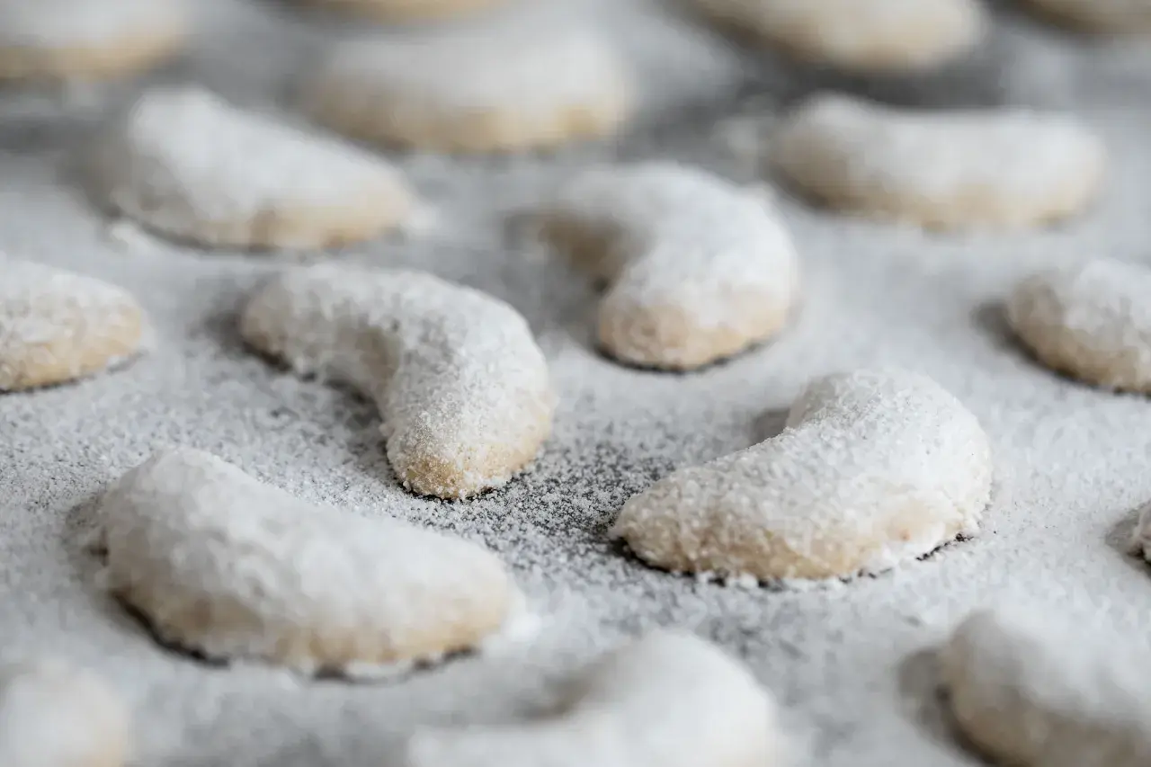 Zarte Vanillekipferl, mit Puderzucker bestäubt, liegen auf einem Blech. Ein süßer Duft liegt in der Luft.